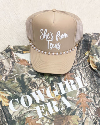 Camouflage shirt with 'Cowgirl fra' text, beige cap, sunglasses, and jeans on a light background
