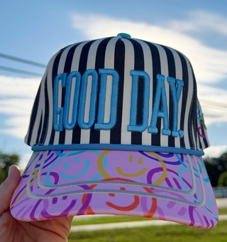 Striped cap with 'GOOD DAY' text held against a blue sky.